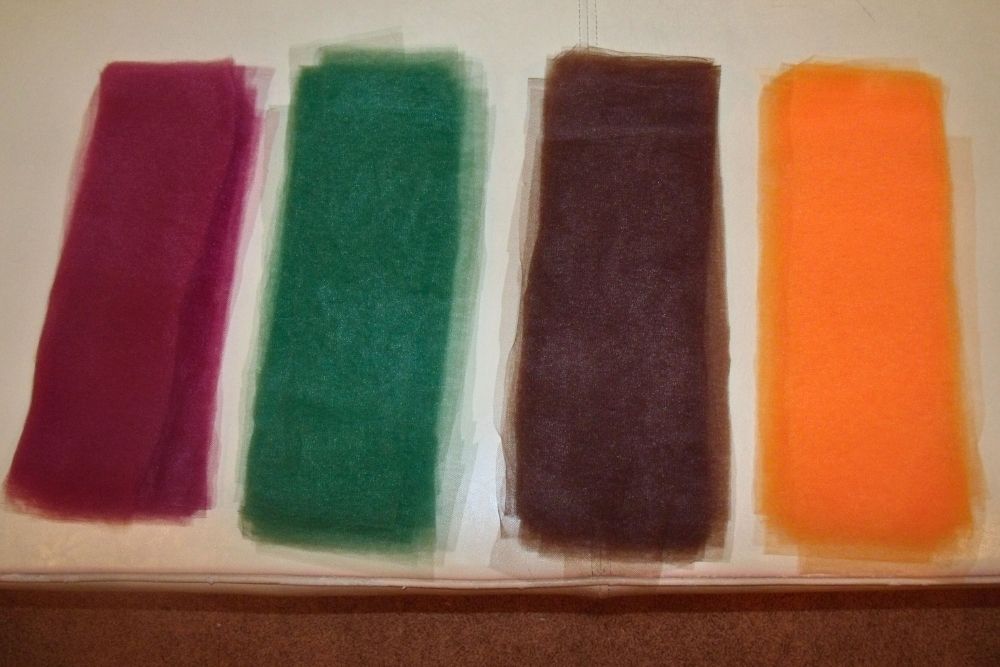 Four piles of tulle in maroon, forest green, dark brown, and marigold orange.