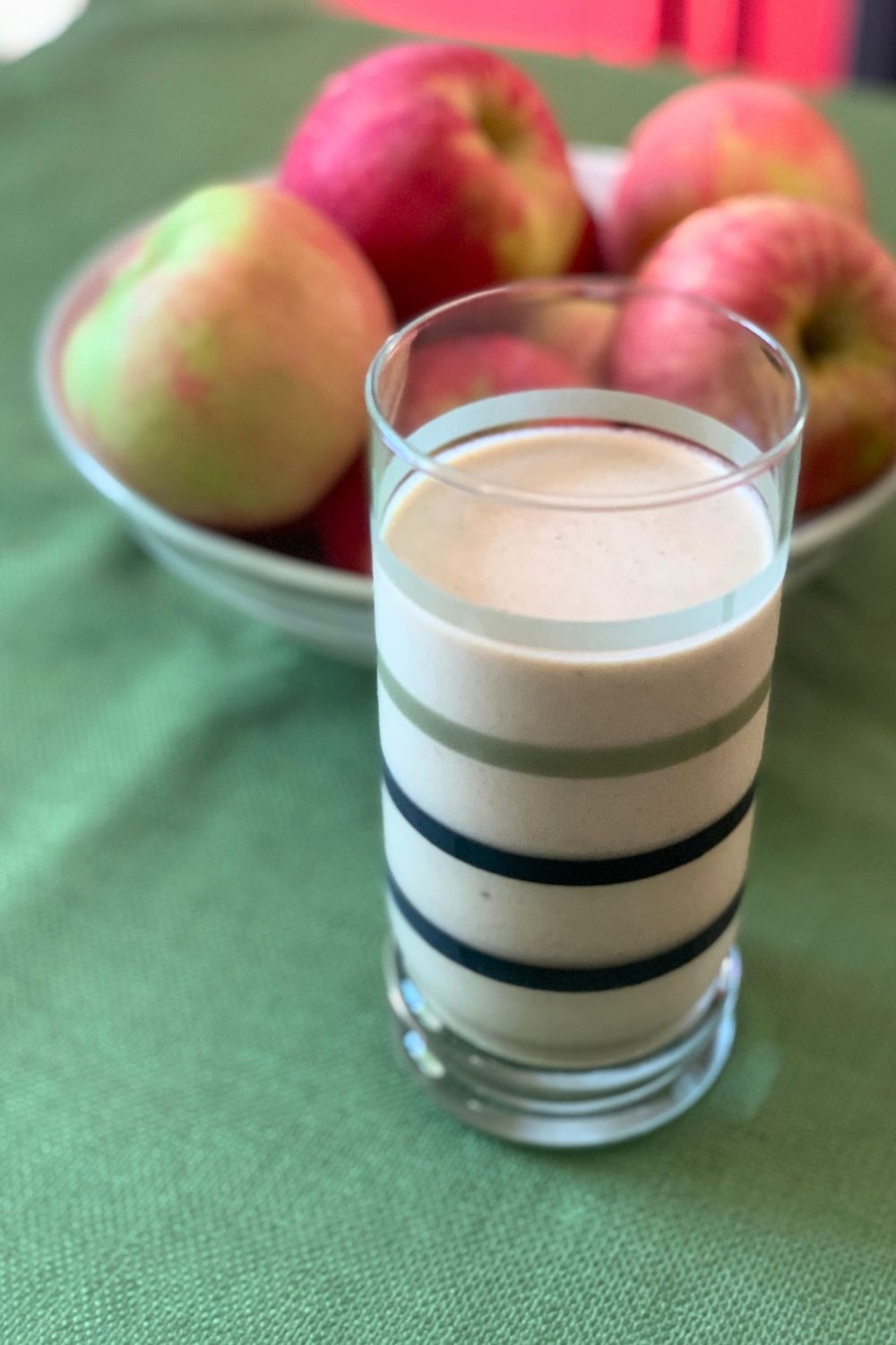 A freshly-made smoothie in a glass beside a bowl of fruit.