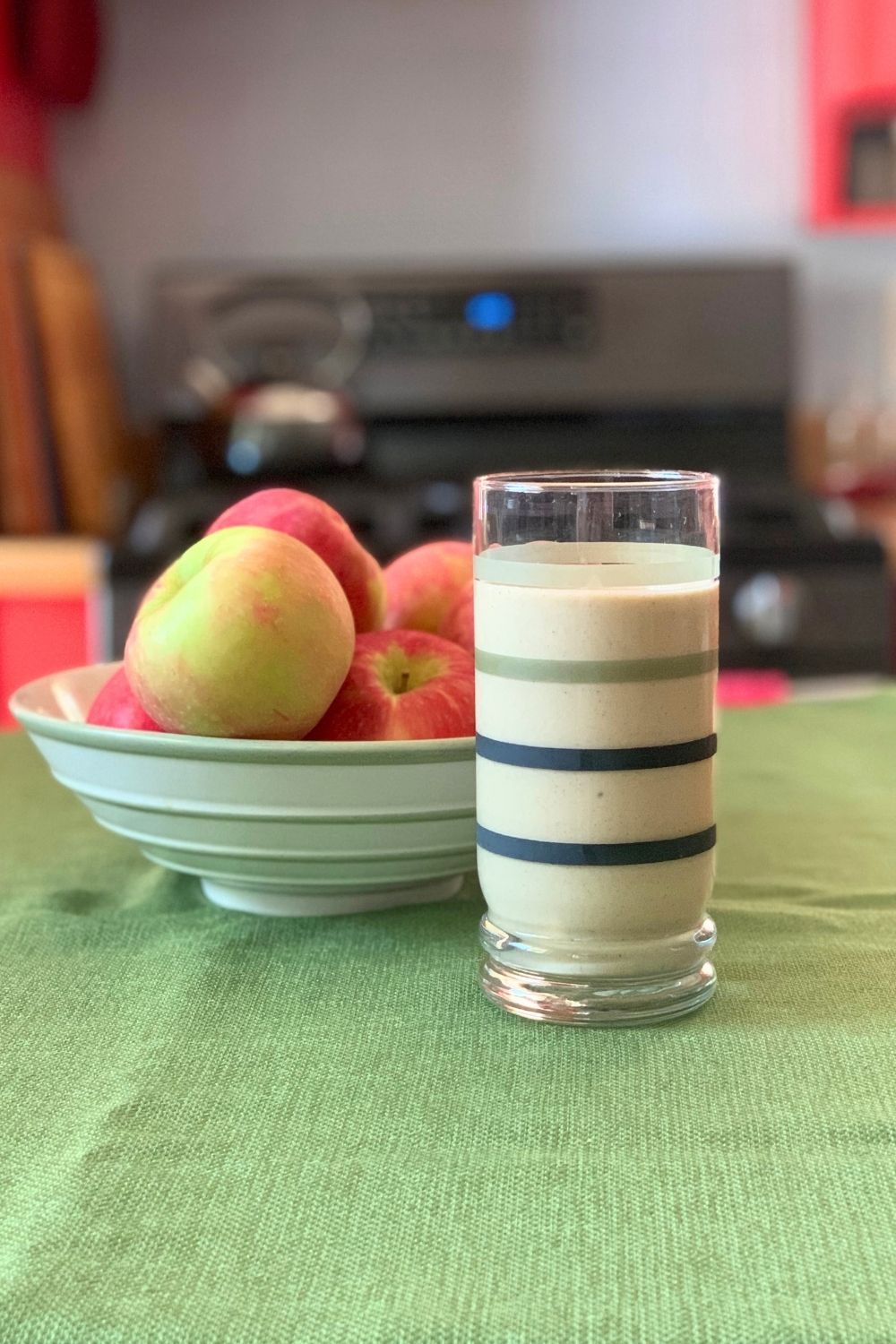 An apple pie smoothie in a glass beside a bowl of fruit.
