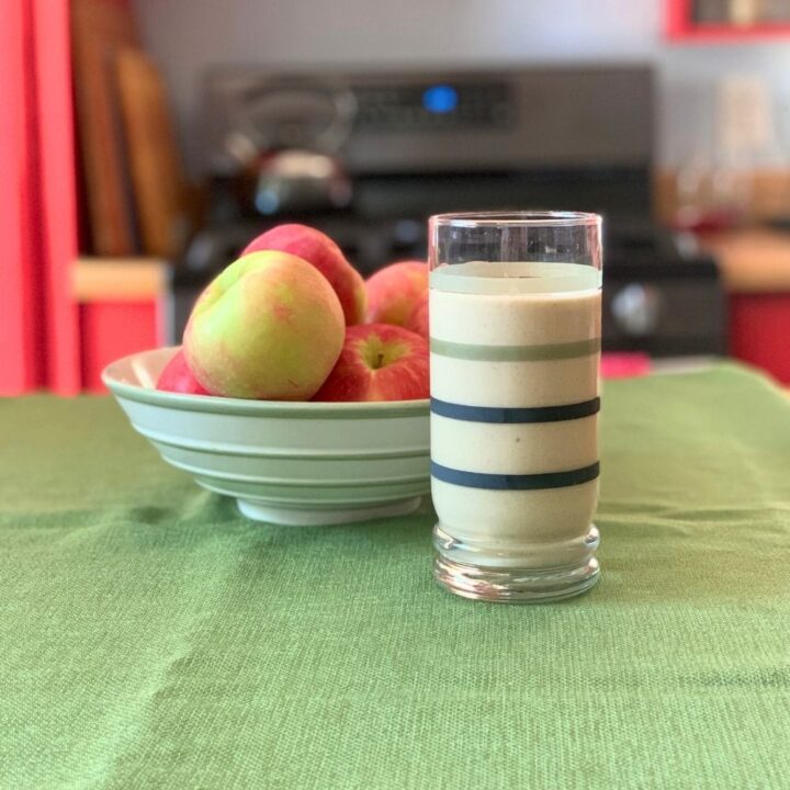 A glass of apple pie smoothie beside a bowl of fruit.