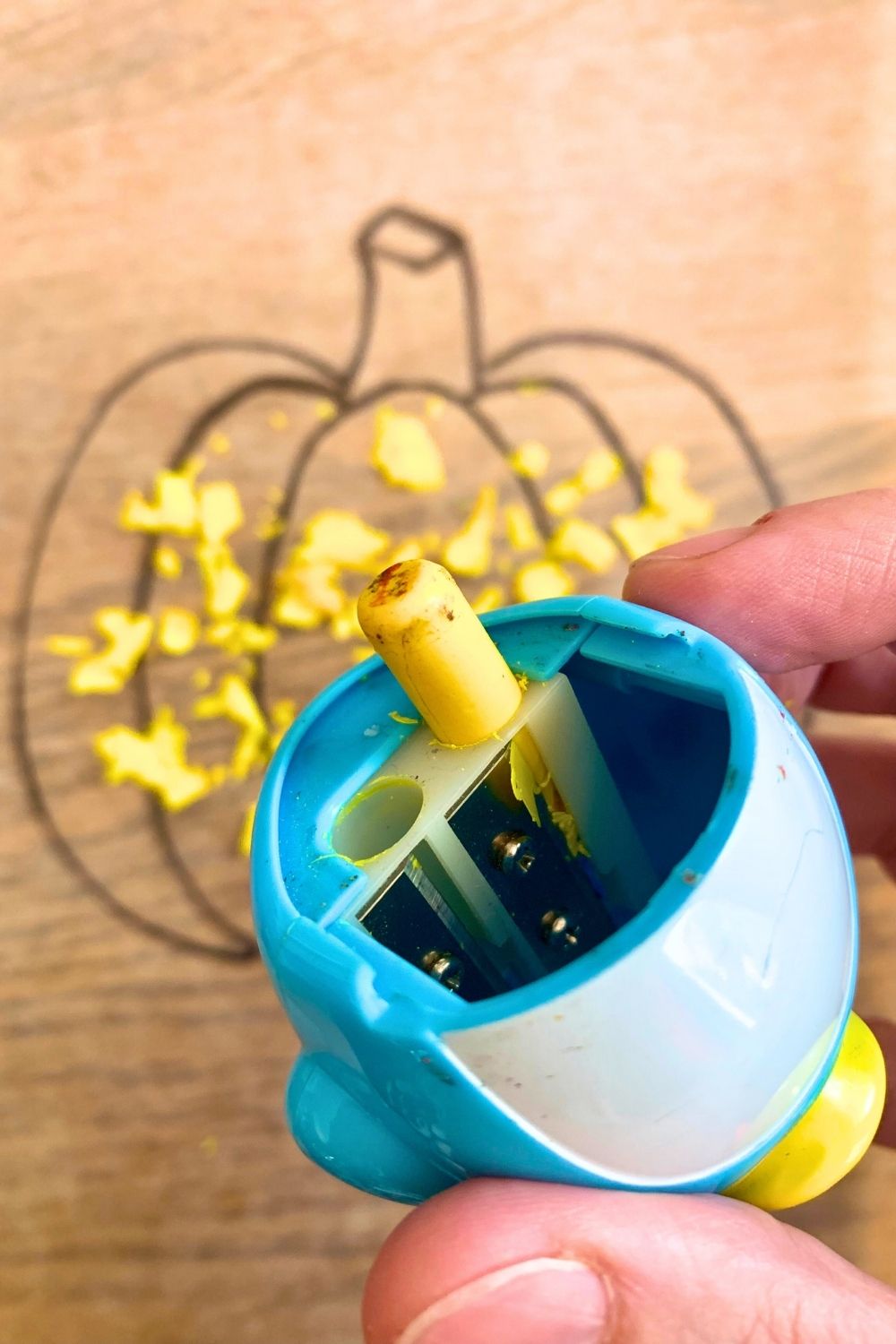 A yellow crayon in a pencil sharpener over a pile of shavings.