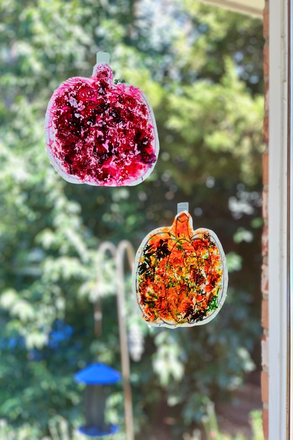 A pink and an orange melted crayon pumpkin stuck to a glass window like sun catchers.