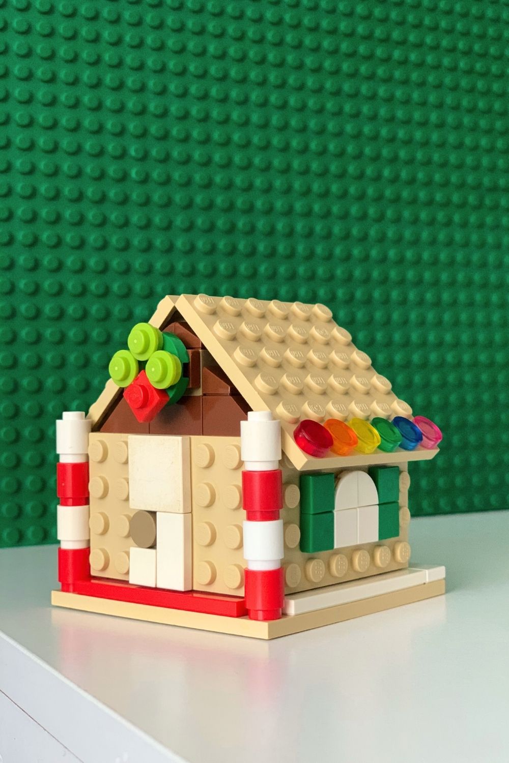 A LEGO gingerbread house made with tan bricks, embellished with flat dots to create a door, window, wreath, and gumdrop trim.