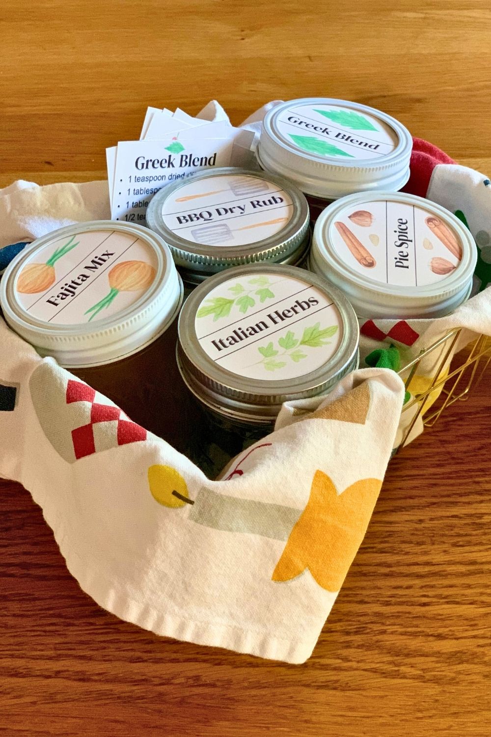 A small basket with a dish towel and 5 pint jars of spice mixes.