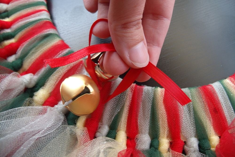 Tying a pair of jingle bells to the Christmas wreath.