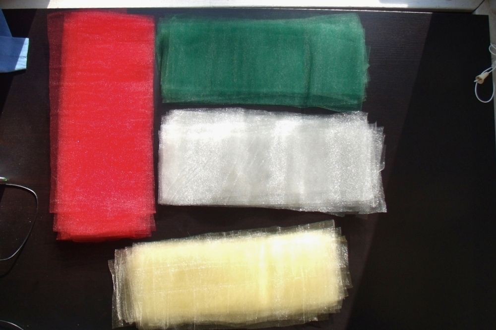 Neat stacks of tulle fabric rectangles in red, green, silver, and gold.
