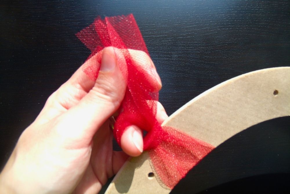 Tying a piece of tulle in a knot to secure it to the frame.