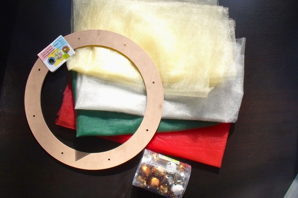 Tulle by the yard in gold, silver, green, and red beside a wreath frame and box of jingle bells.