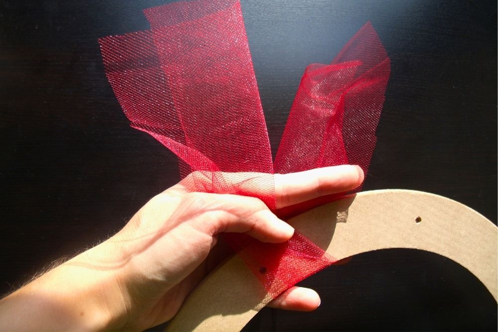 Folding a piece of red tulle around a wreath frame.