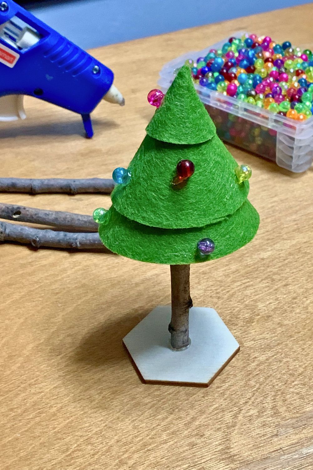 A green felt Christmas tree with a stick trunk, decorated with colorful beads as ornaments.