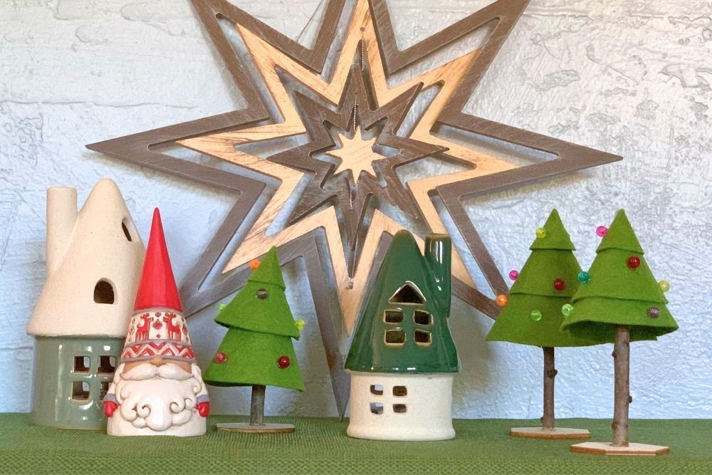 A tabletop setup with Christmas trees, ceramic houses, and a Scandinavian-style gnome in front of a giant wood star.