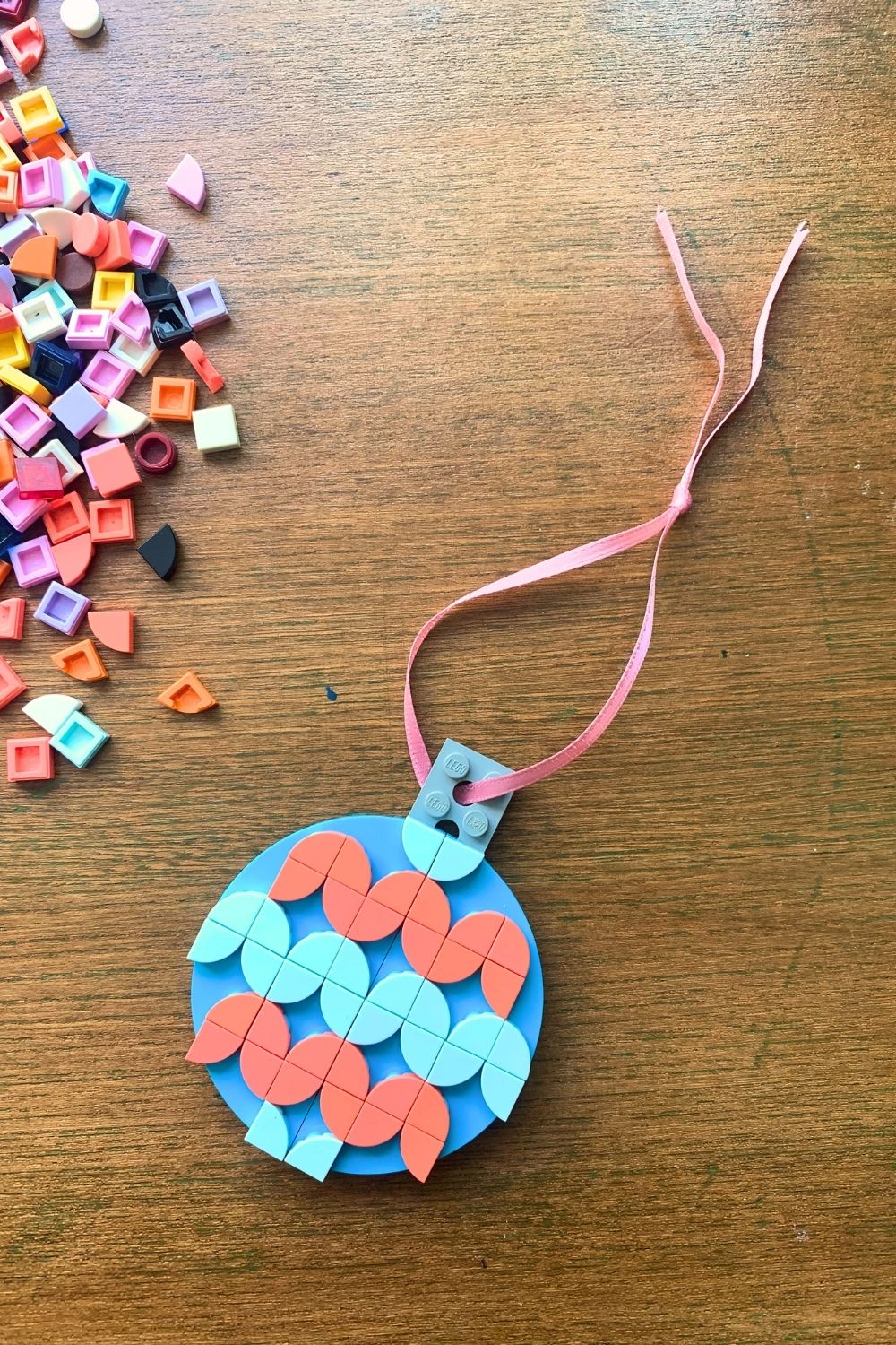 A Christmas ornament made from a flat blue LEGO circle decorated with pink and blue wedge dots.