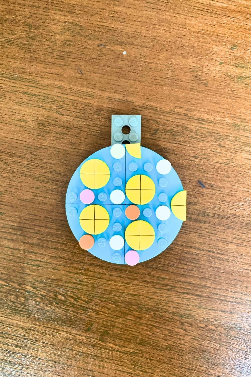 A blue LEGO ornament decorated with yellow, white, orange, and pink dots in multiple sizes.