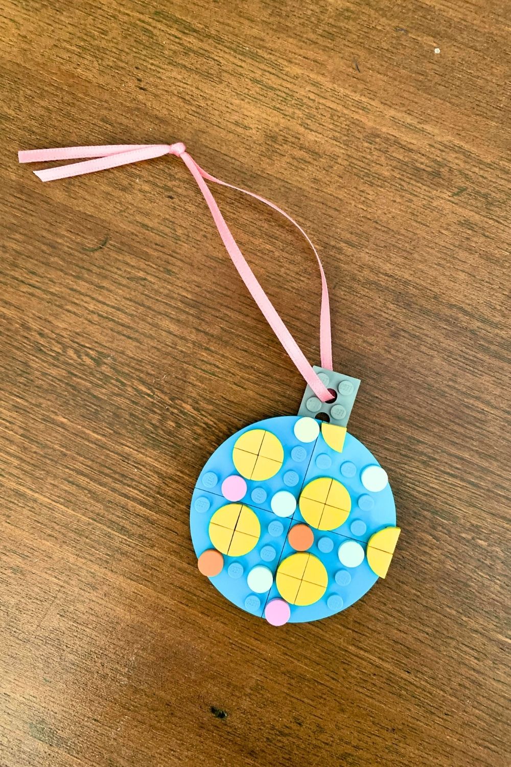 A blue LEGO ornament decorated with dots and a ribbon tied through a brick with a hole at the top.