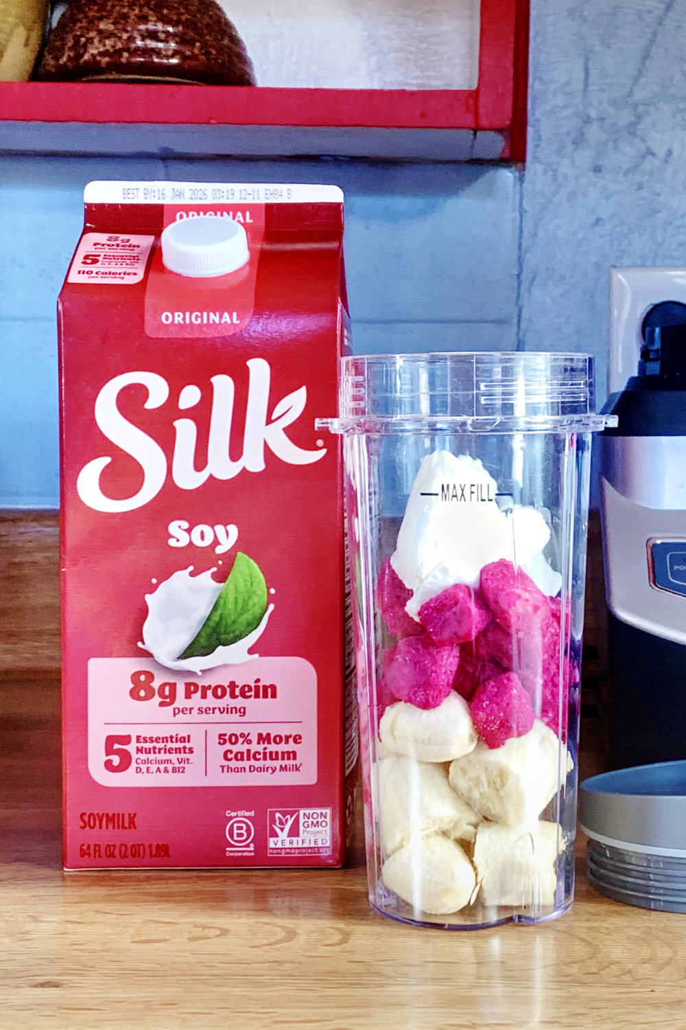 A carton of silk soy milk beside a clear cup of dice banana, dragonfruit, and yogurt.