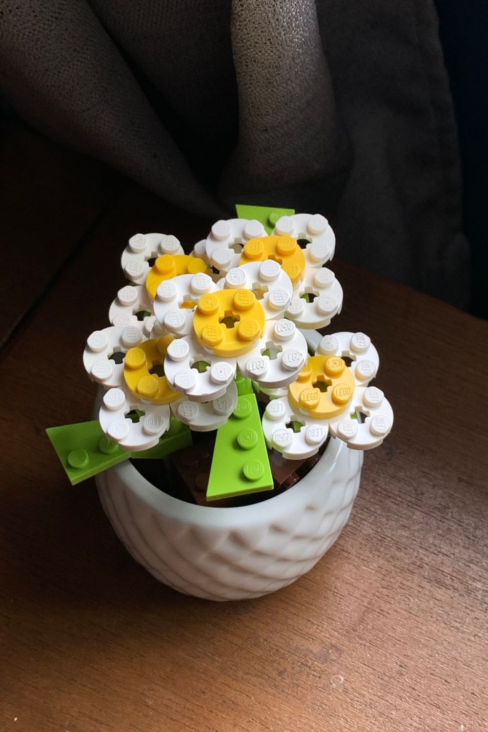 A small flower pot of white LEGO daisies with yellow centers and green leaves.