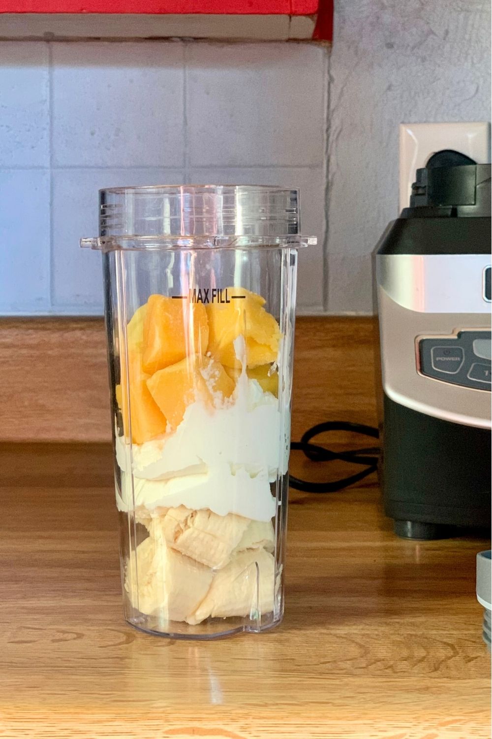 A smoothie cup filled with banana chunks, yogurt, and diced mango.