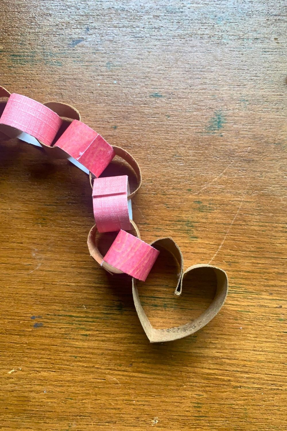 A brown paper tube heart attached to half a dozen tiny paper rings.