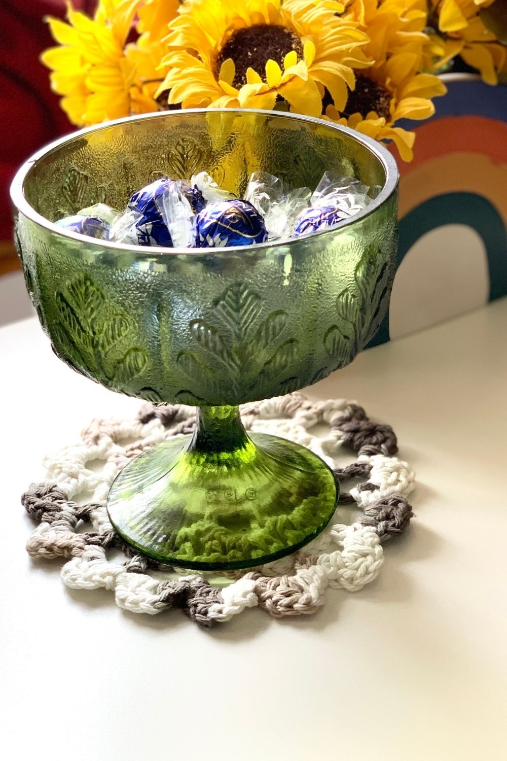 A brown and white crochet doily on an end table under a glass candy dish.