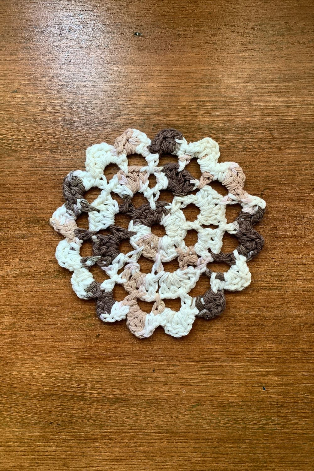 A brown and white crochet doily on a wood table.