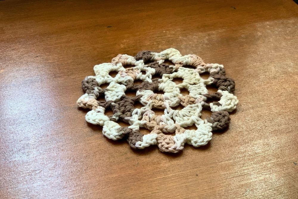 A white and brown crochet doily on a wood table.