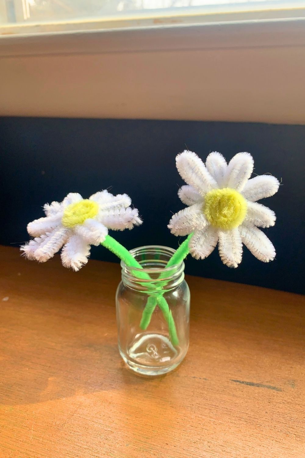 A pair of white pipe cleaner daisies with yellow centers and green stems.