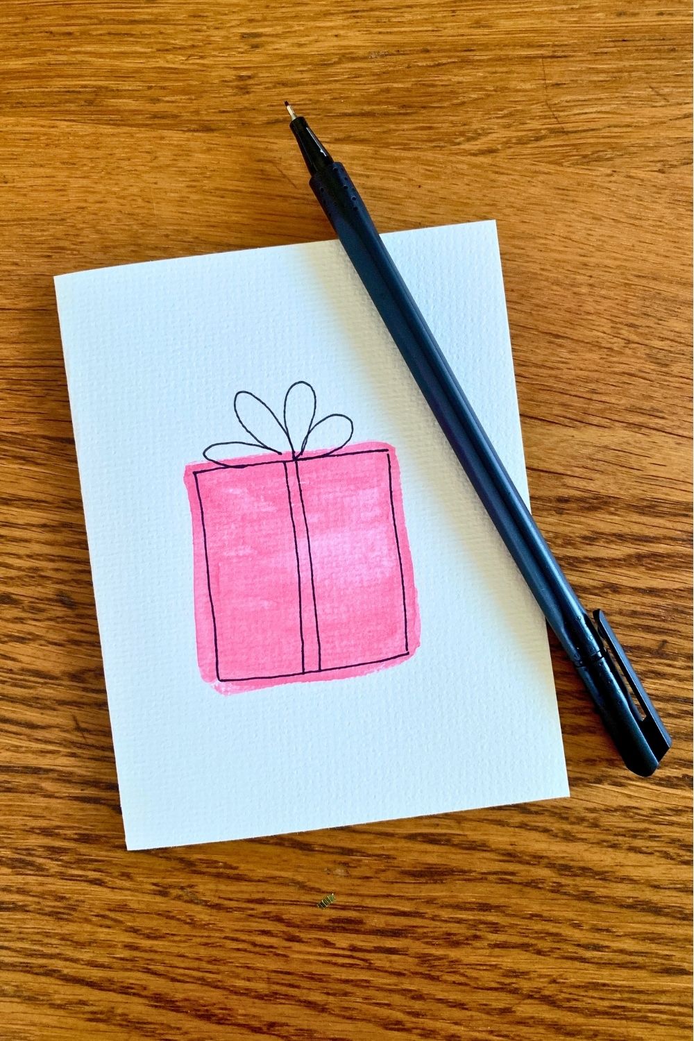 Outlining a painted square with black pen to resemble a wrapped gift with a bow.