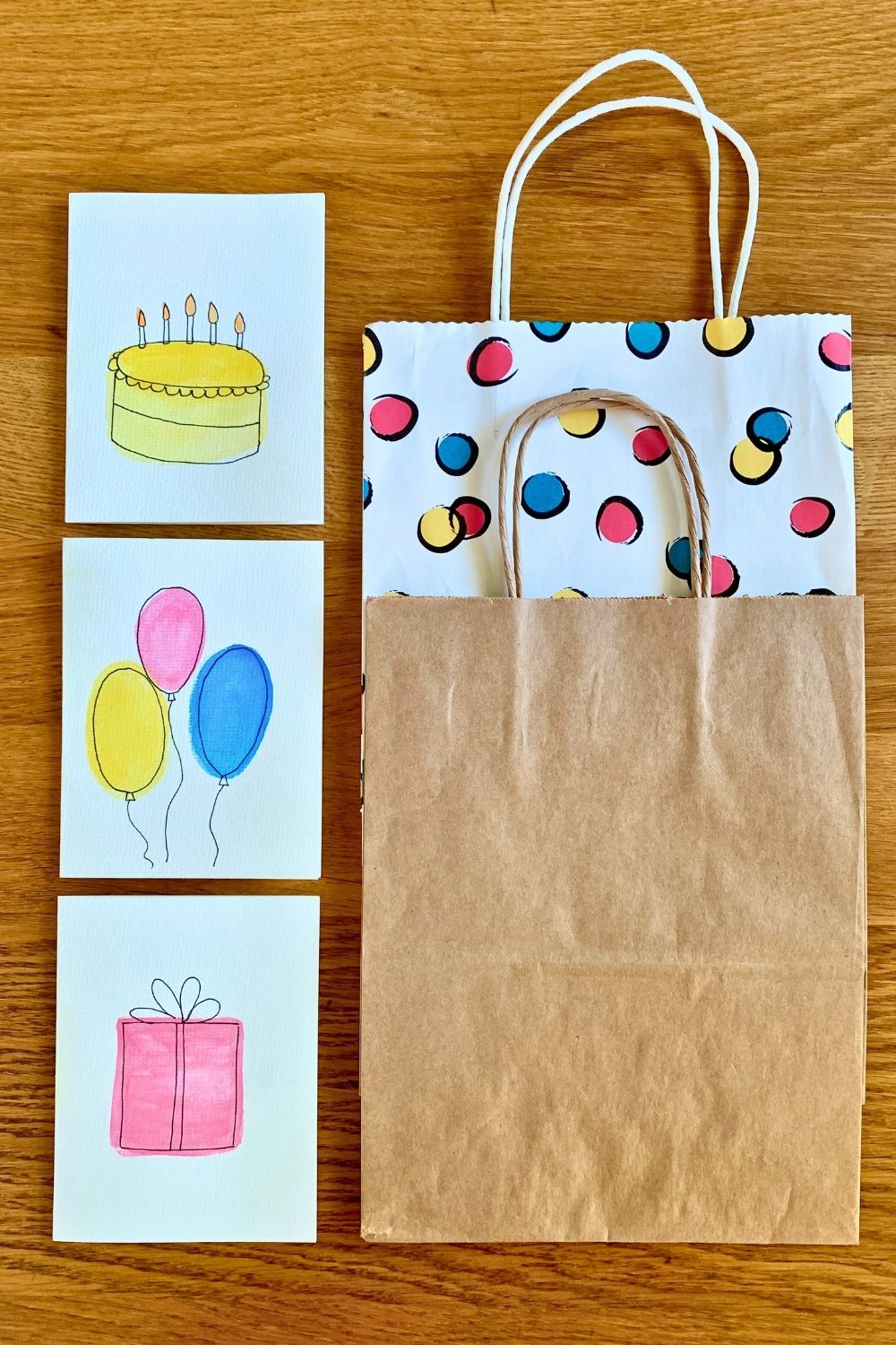 Handmade watercolor birthday cards with illustrations of a yellow cake, pastel balloons, and a pink wrapped gift.