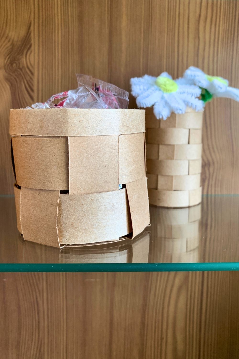 Small paper baskets made from woven kraft paper holding peppermints and faux flowers.