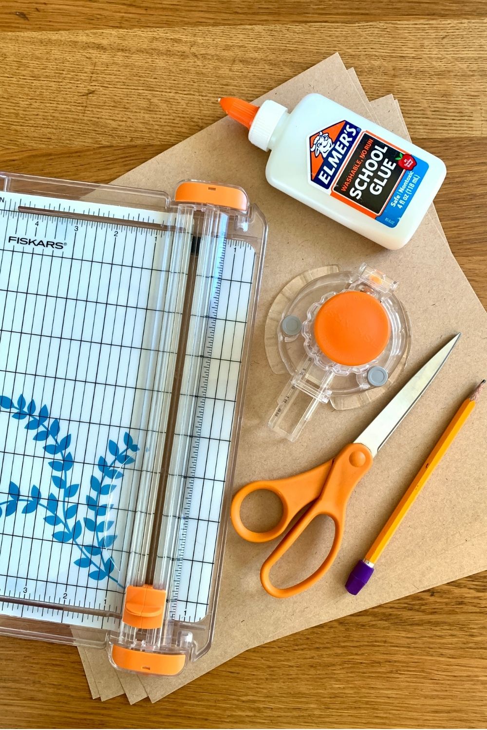 Brown kraft paper, a flat paper trimmer, a circle paper cutter, scissors, pencil, and school glue.