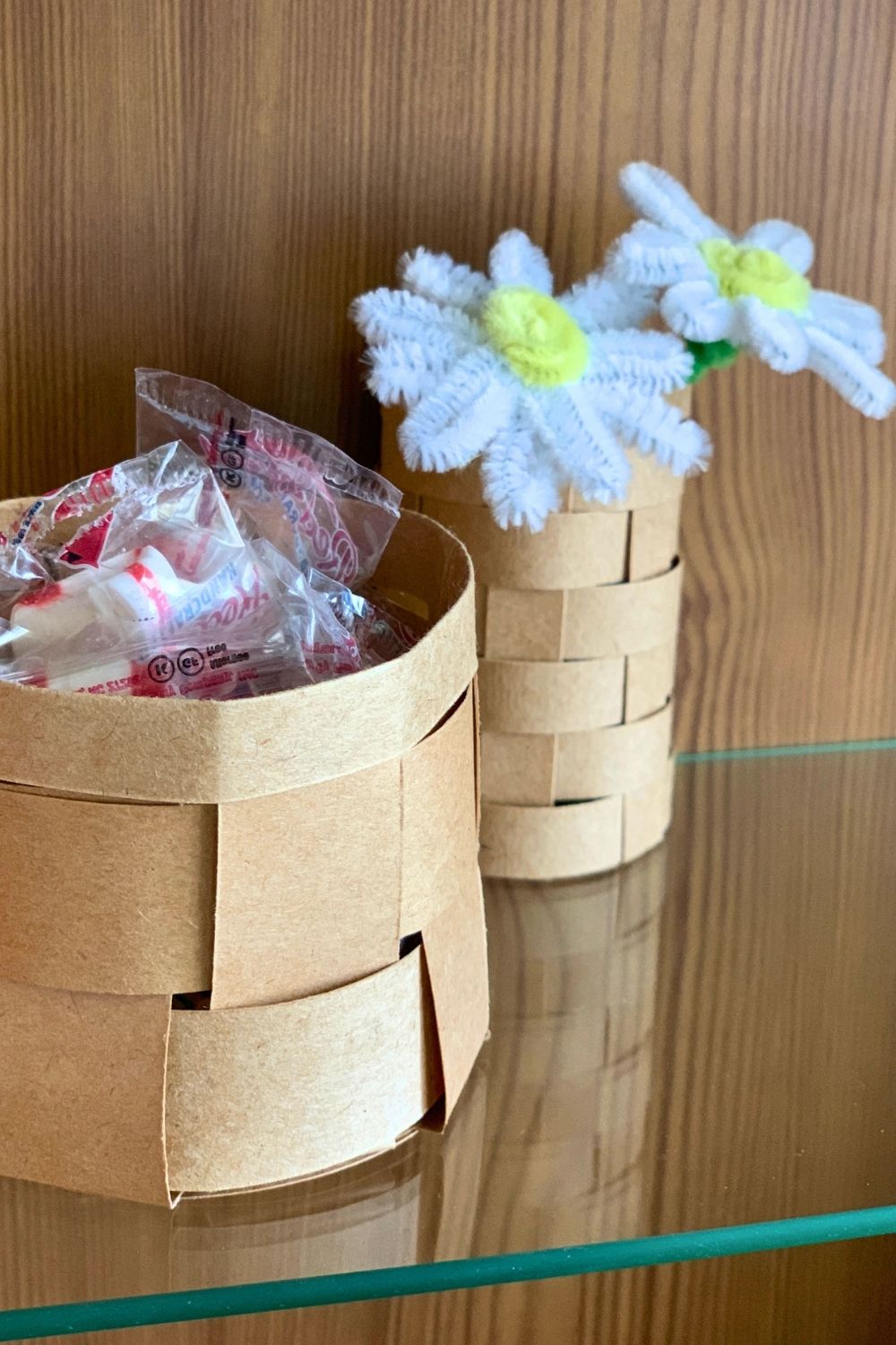 Small paper baskets made from woven kraft paper holding peppermints and faux flowers.