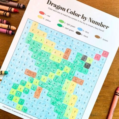 Printable dragon color by number with green, yellow, and blue boxes colored with crayons.