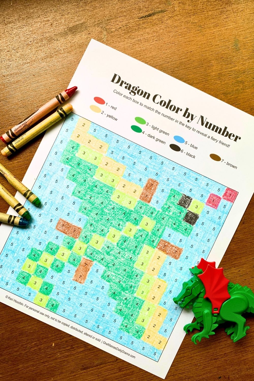 Printable dragon color by number with green, yellow, and blue boxes colored with crayons.