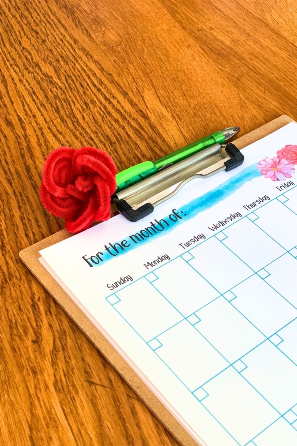 Pipe cleaner rose on the top of a green pen beside a calendar.