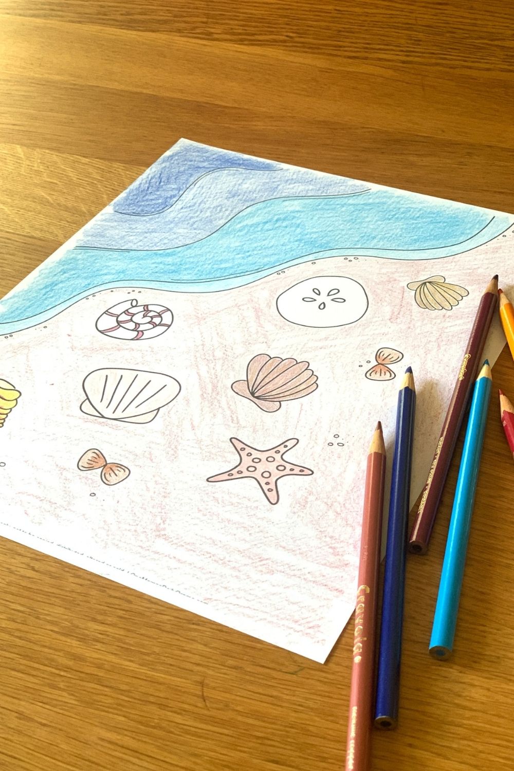 Coloring the ocean water in shades of blue with pencils.