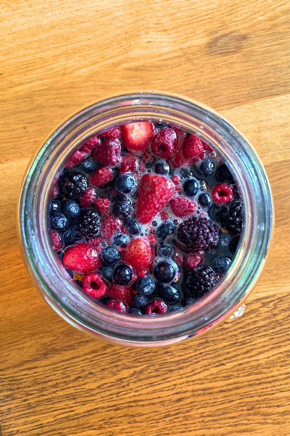 Mixed berries floating in liquid in a glass container.