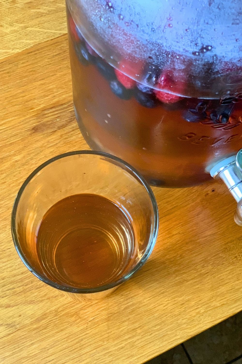A glass of summer punch beside a filled glass dispenser.