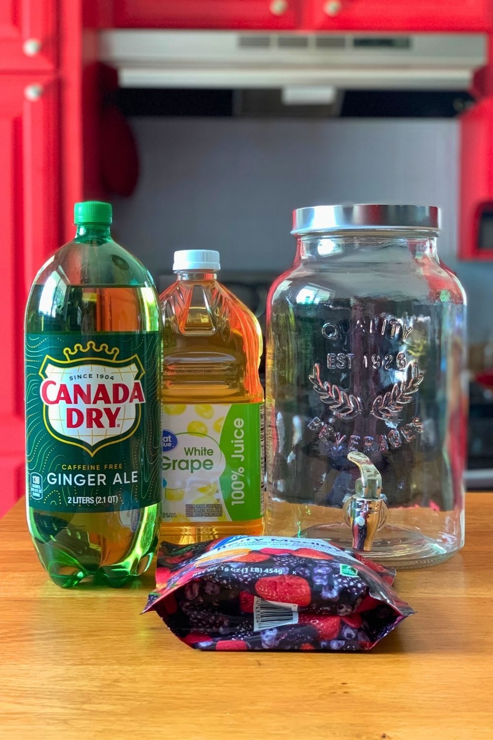 A 2-liter ginger ale, 2-quart white grape juice, and bag of frozen berries beside a glass dispenser.