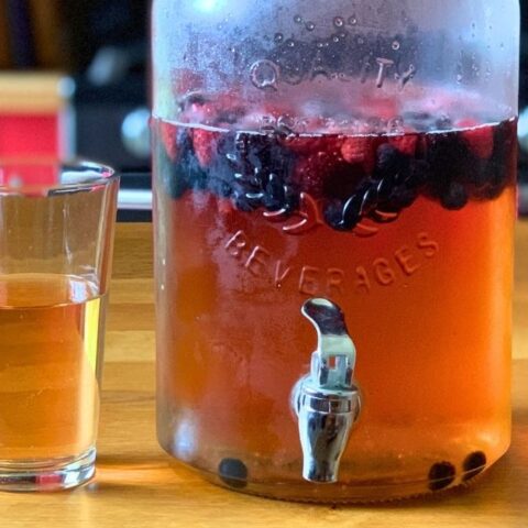 Summer punch with a golden pink liquid and berries floating in a dispenser beside a filled glass.