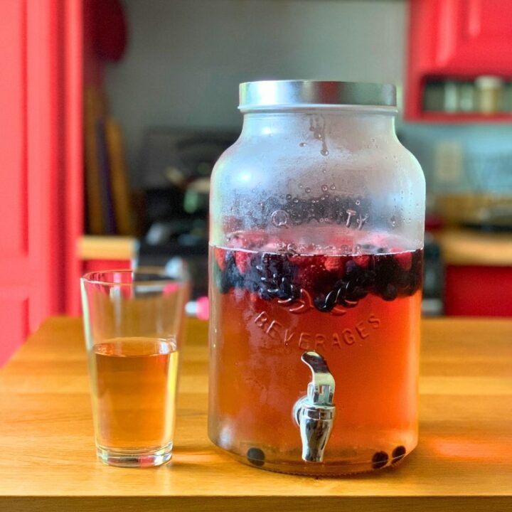 A glass dispenser of summer punch with mixed berries floating in a pink liquid.