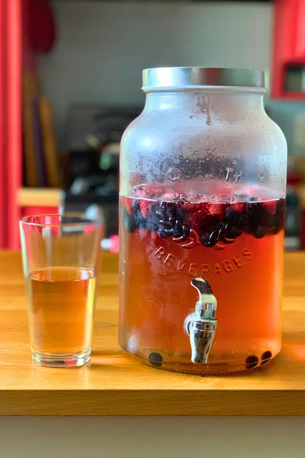Summer punch with a golden pink liquid and berries floating in a carafe beside a filled glass.