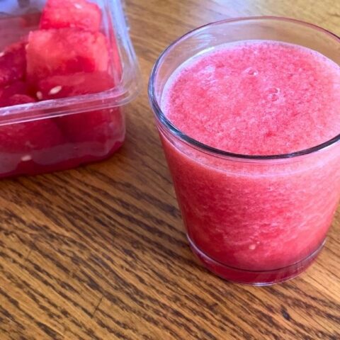 A glass of watermelon slush beside a container of fruit chunks.