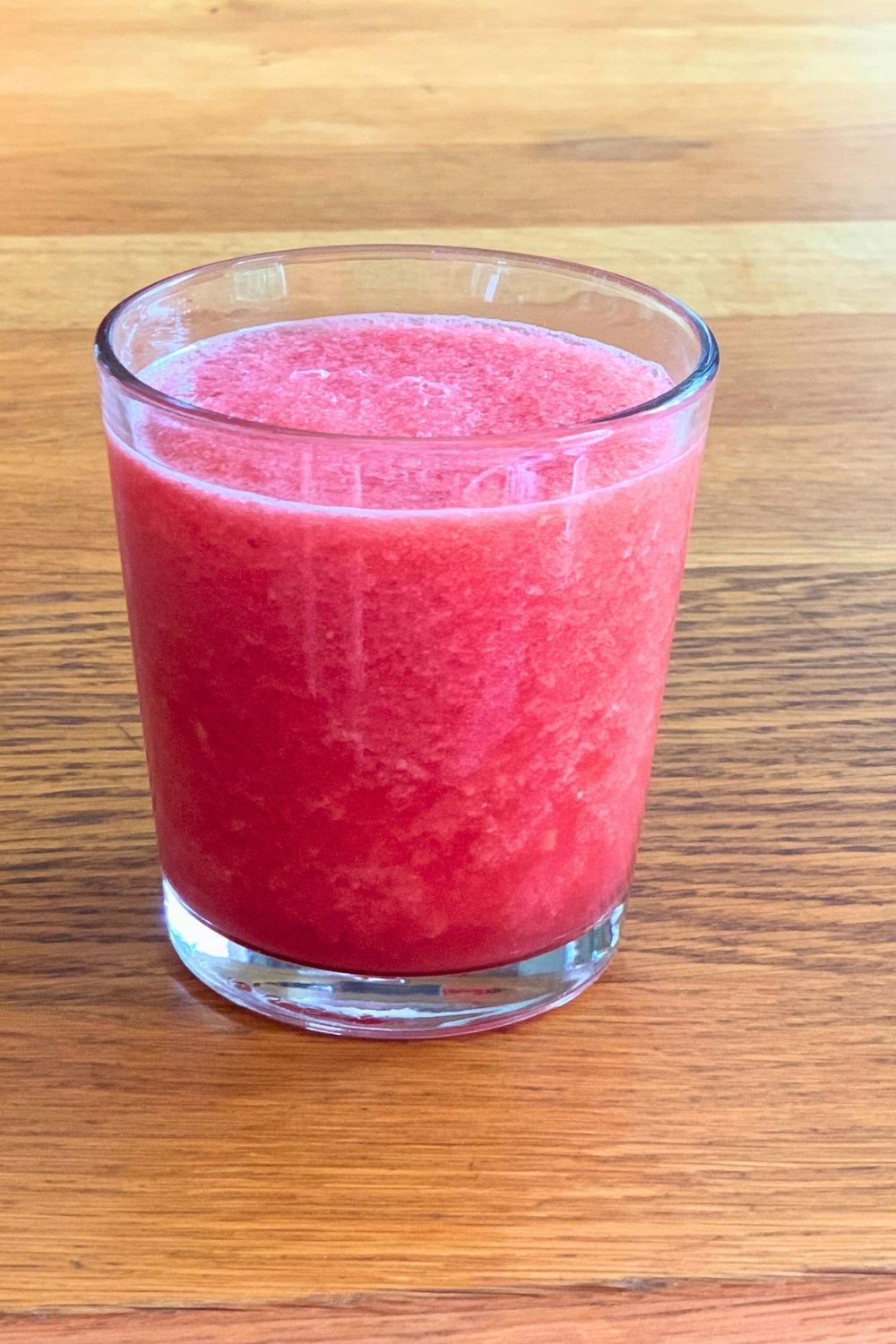 A glass of watermelon slush beside a container of fruit chunks.