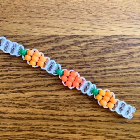 A pumpkin bracelet made from orange, green, and clear pony beads on cord.