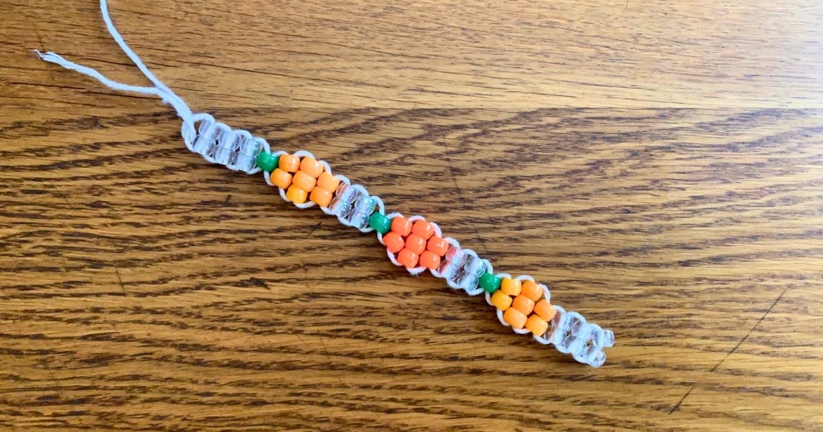 A pumpkin bracelet made from orange, green, and clear pony beads on cord.