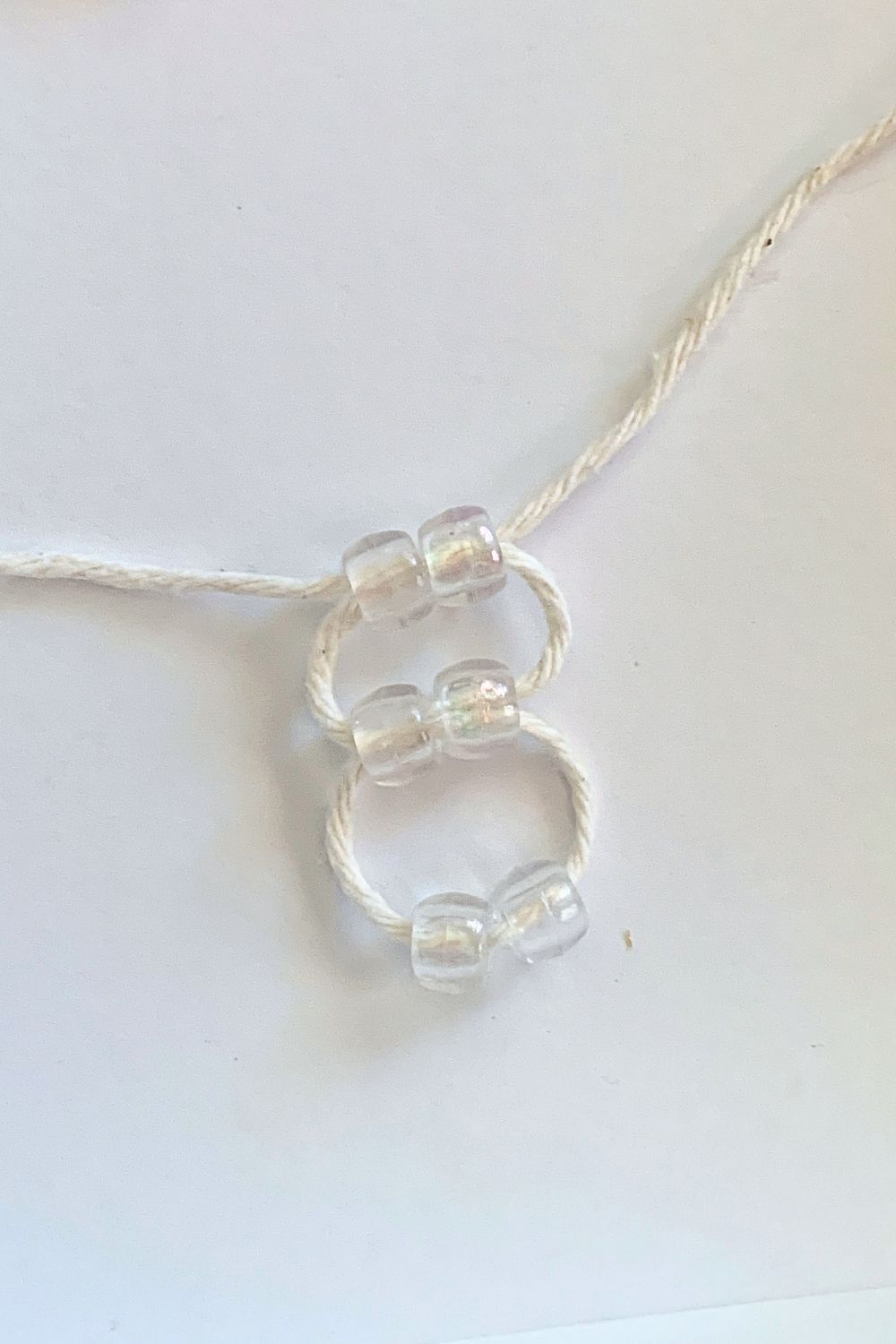 Weaving 3 sets of 2 clear pony beads on white cord.