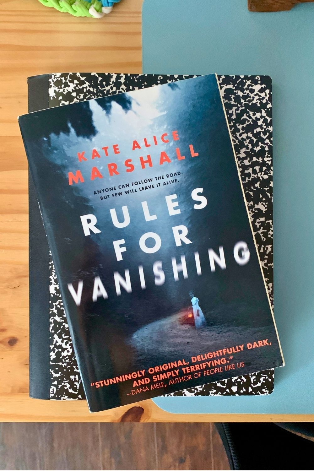 A paperback of Rules for Vanishing by Kate Alice Marshall on top of a composition book.