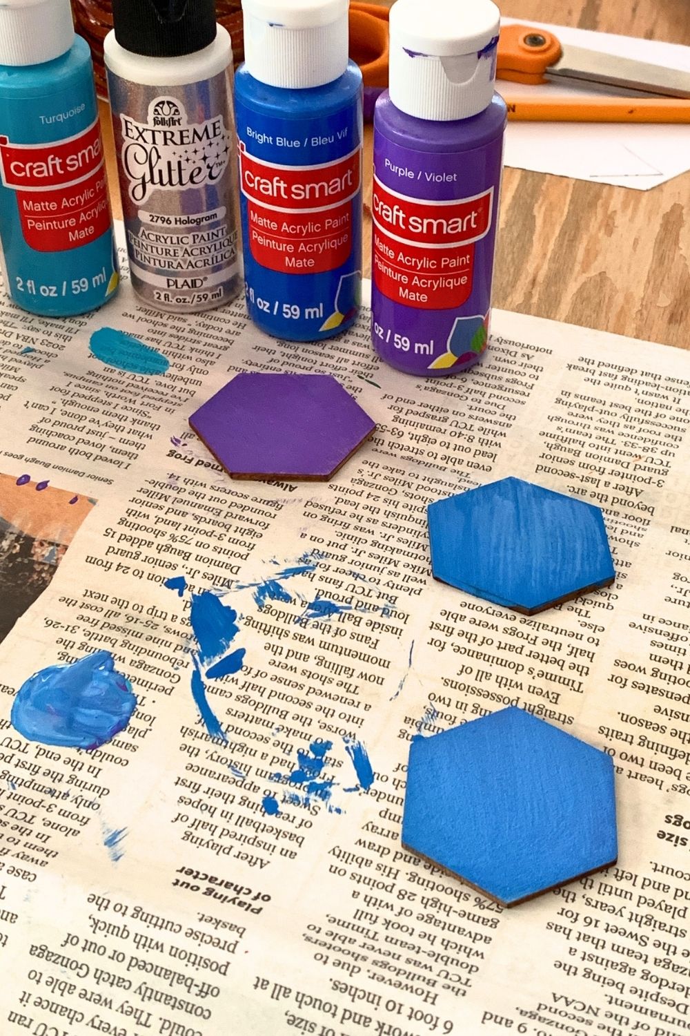 Flat painted hexagons in blue and purple on newspaper beside bottles of paint.