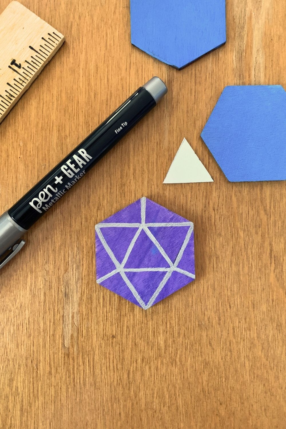 A purple hexagon with triangles and lines painted in silver marker.