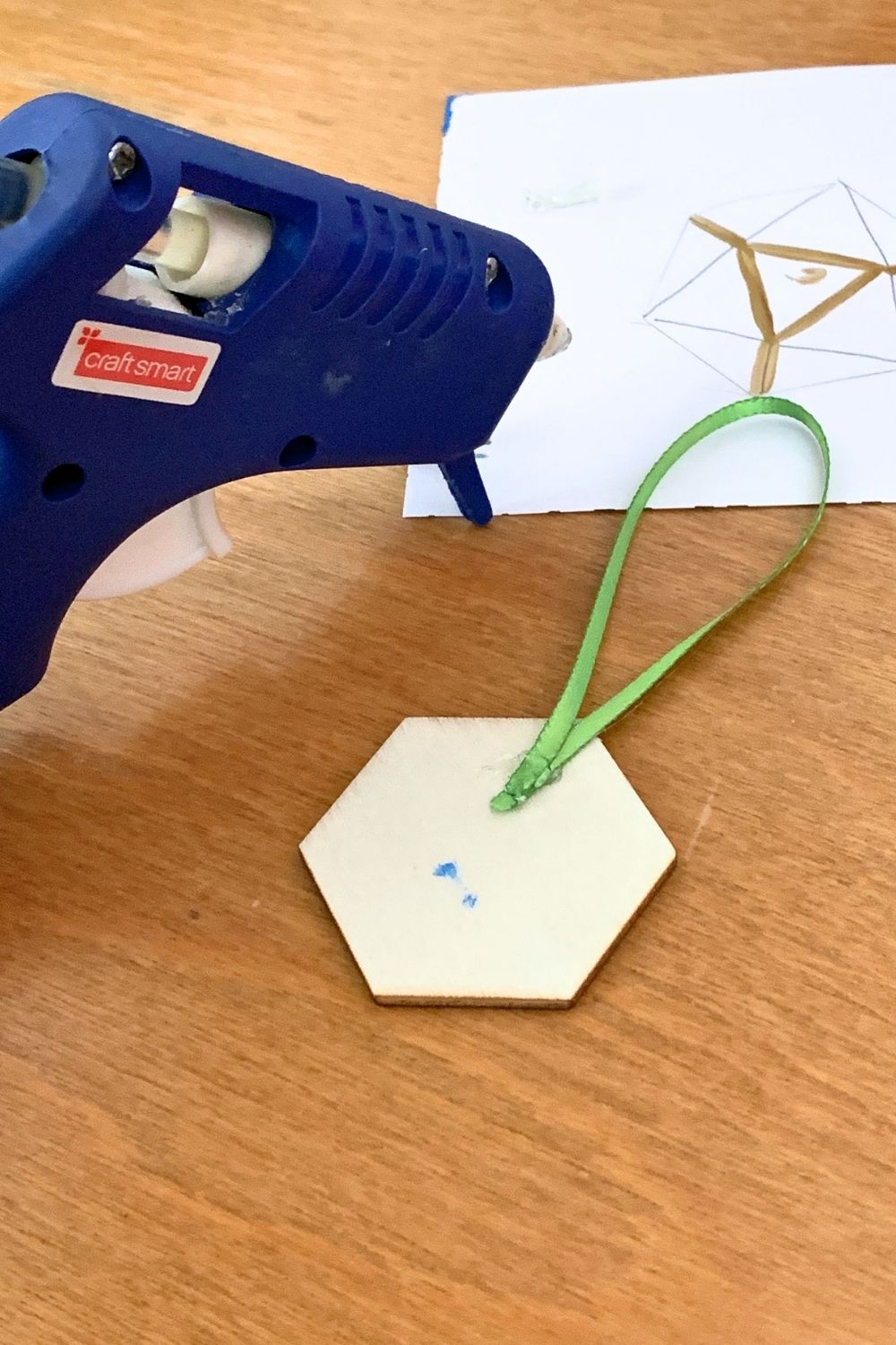 Gluing a looped green ribbon to the back of a wooden hexagon.
